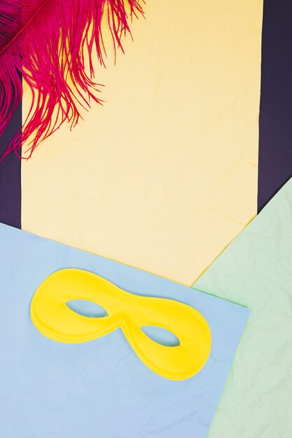 Pink feather and yellow eye mask against colorful paper