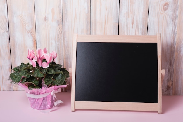 木製の壁の机の上に小さな空白の黒板とピンクの花束