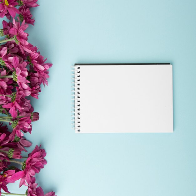 Pink flowers border and blank spiral notepad on blue background