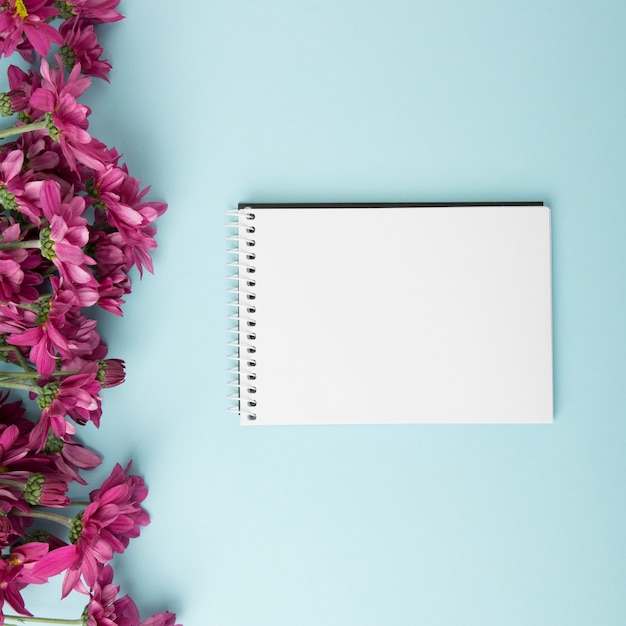 Pink flowers border and blank spiral notepad on blue background