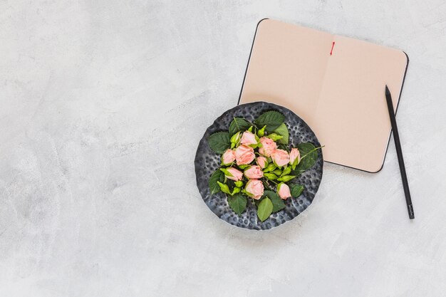 Pink flowers on circular tray with diary and pencil on concrete background