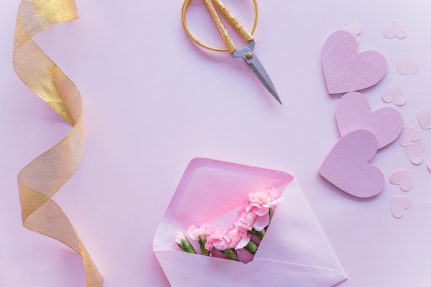 Pink flowers in envelope with paper hearts on table 