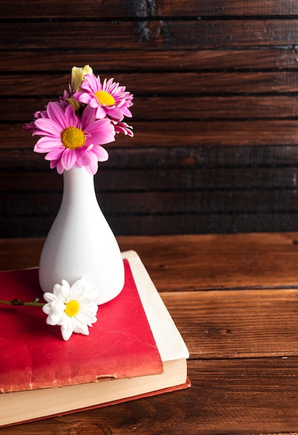 Pink flowers in white vase on book 