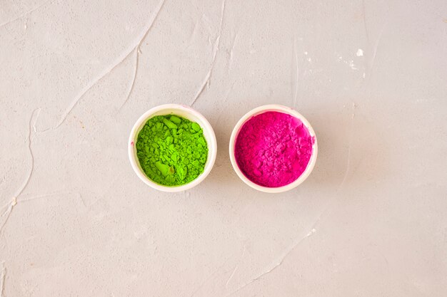 Foto gratuita polvere di colore rosa e verde di holi in ciotola bianca su fondo concreto