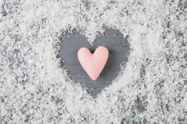 Бесплатное фото Розовое сердце между декоративным снегом на деревянном столе