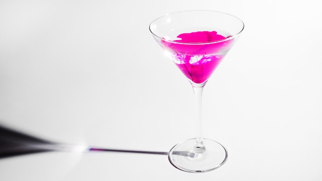 Розовые чернила, растворяющиеся в бокале для мартини на белом фоне