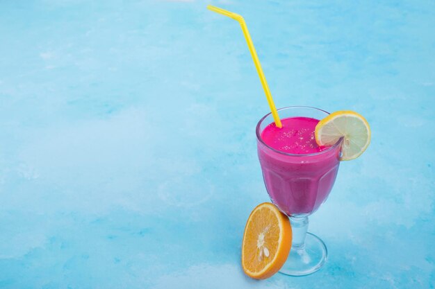 Pink juice in a glass cup with yellow pipes on blue background. High quality photo