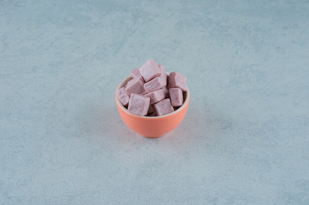 Pink marshmallow candies in a bowl on white surface