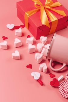 Pink mug on a pink background filled with marshmallows in the form of hearts. next to it is a box with a gift for valentine's day. valentine's day holiday concept