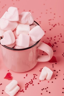 Pink mug on a pink background filled with marshmallows in the form of hearts. valentine's day holiday concept