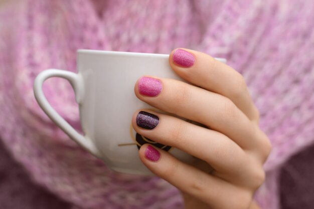 Pink nail design. Female hand holding white cup.