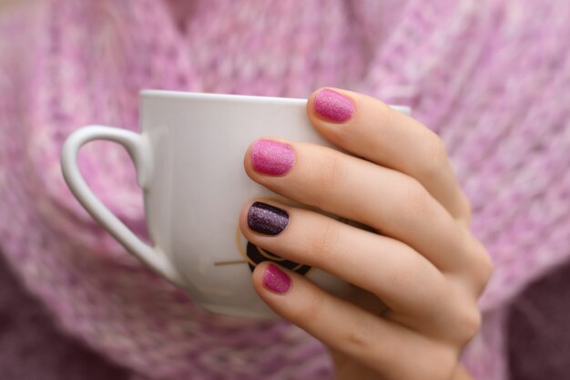 ピンクのネイルデザイン。白いカップを持っている女性の手。