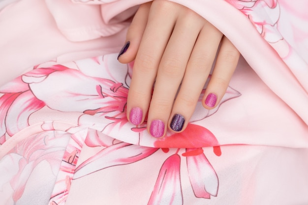 ピンクのネイルデザイン。キラキラのマニキュアで女性の手。