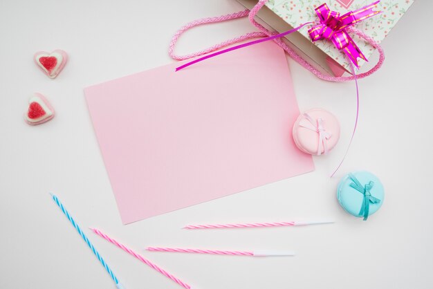 Pink paper; macarons; candles and heart shape candies and shopping bag on white background