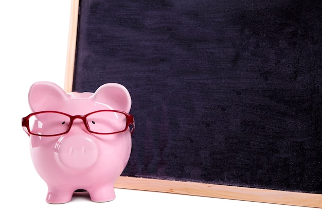 Pink piggy bank with glasses standing next to a blackboard 