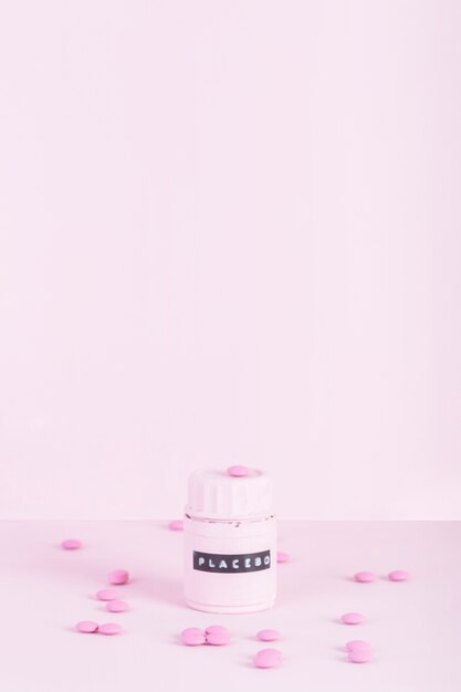 Pink pills surrounded with placebo closed bottle over pink background