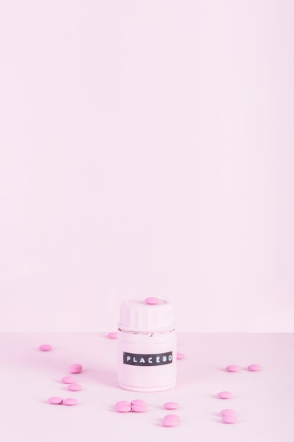 Pink pills surrounded with placebo closed bottle over pink background