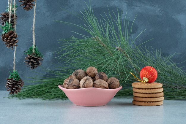Розовая тарелка, полная грецких орехов и сладкого печенья на мраморном фоне. Фото высокого качества