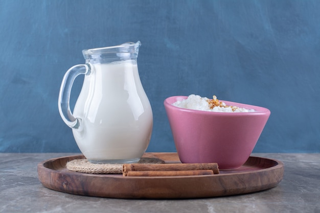 A pink plate of healthy oatmeal porridge with a glass jug of milk and cinnamon sticks on a wooden board. 