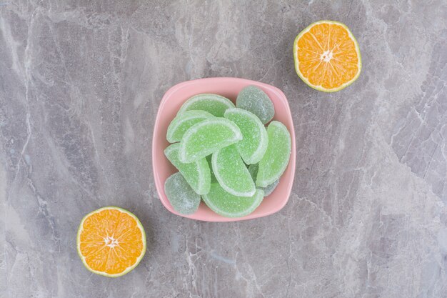 A pink plate of marmalades and slice of orange on marble background.