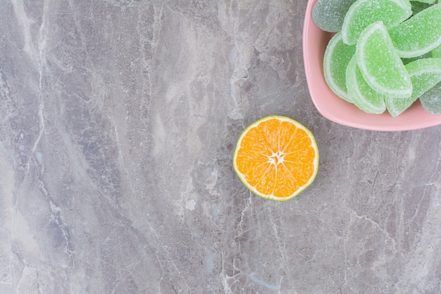 A pink plate of marmalades and slice of orange on marble background.