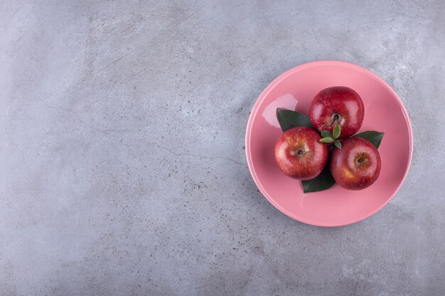 Pink plate of ripe red apples placed on stone.