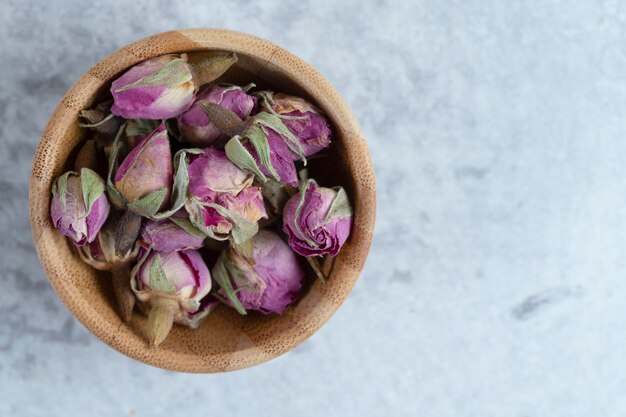 Pink red dried rose buds in a wooden bowl with petals placed on a stone background . High quality photo