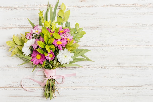 木製の机の上の花の花束と結ばれるピンクのリボン