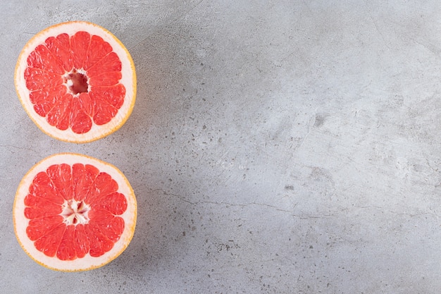 Pink ripe grapefruit slices placed on a stone table.