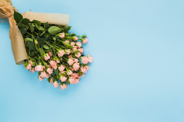 青い背景に茶色の紙に包まれたピンクのバラの花束