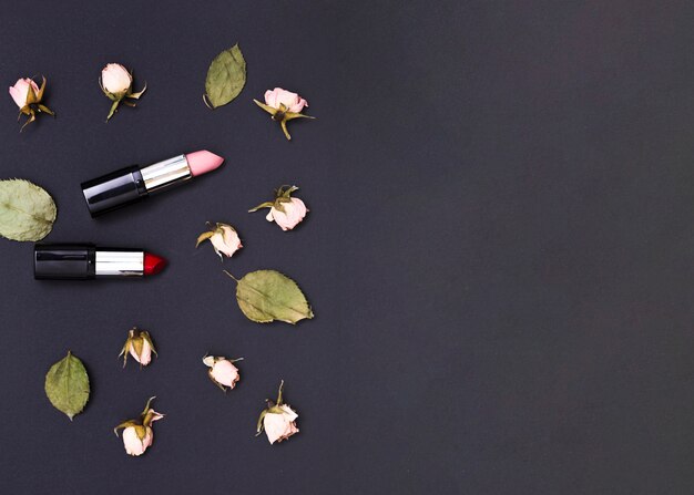 Pink rose buds and green leaves with an open red and pink lipsticks on black background