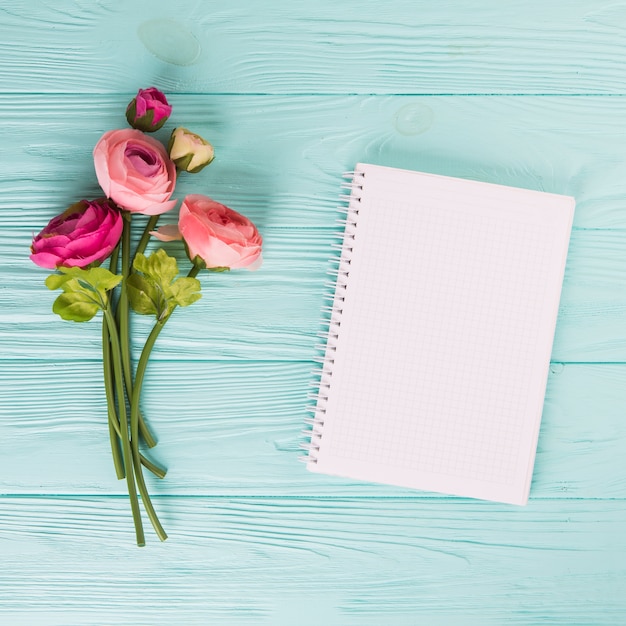 木製のテーブルの空白のノートブックとピンクのバラの花
