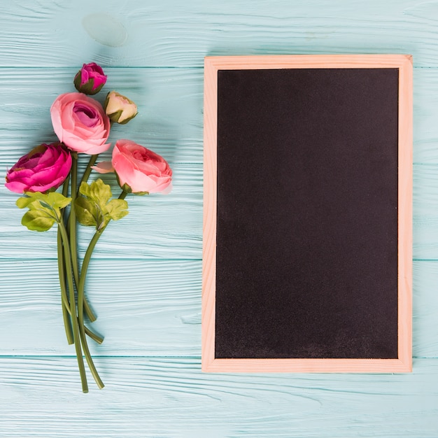 Free photo pink rose flowers with chalkboard on blue wooden table