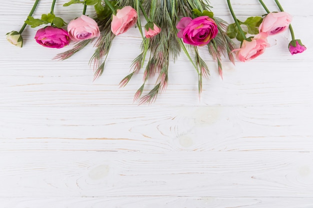 Pink rose flowers with green plant branches on wooden table 