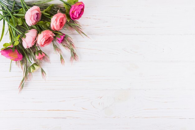 Pink rose flowers with plant branches on wooden table 