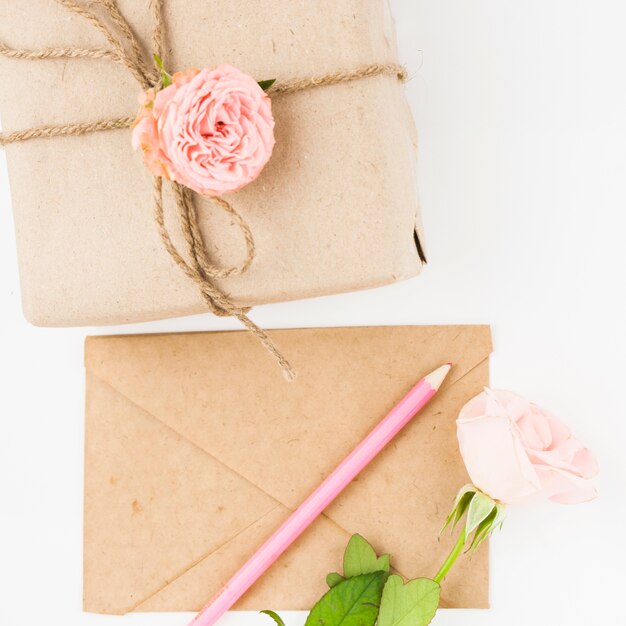 분홍 장미; 갈색 종이 봉투와 소포에 연필 흰색 배경에 대해 문자열로 묶어