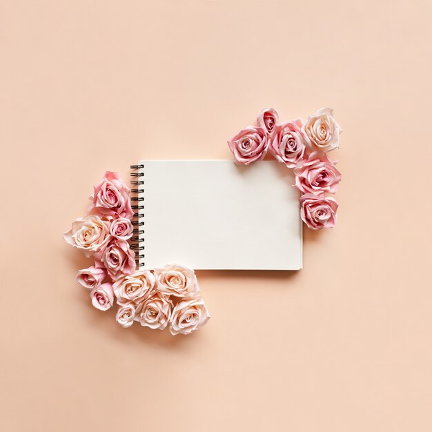 Pink roses are lined around a notebook on a light pink background.