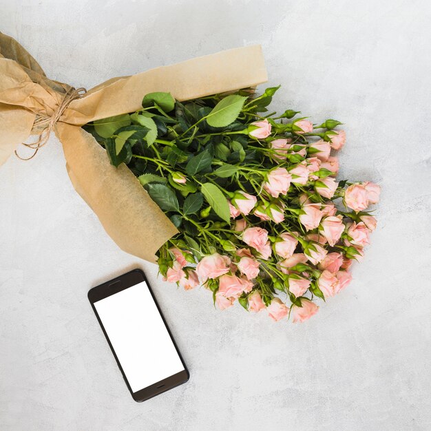 Pink roses bouquet wrapped in brown paper and smartphone on concrete backdrop