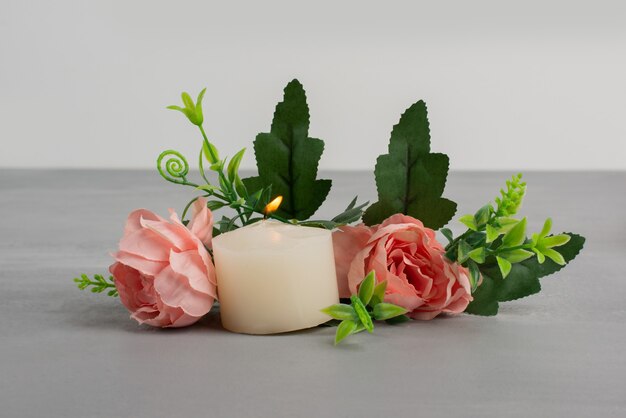 Pink roses with green leaves and candle on grey table.