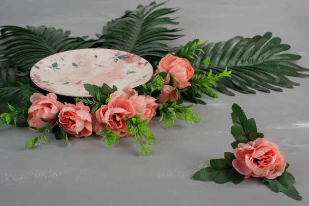 Pink roses with green leaves and plate on grey surface.