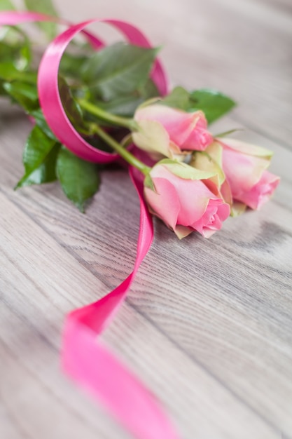 Free photo pink roses with ribbon on wood