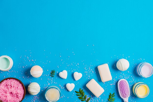 Pink salt bowl; bath bomb; soap; hairbrush and moisturizer cream on blue background