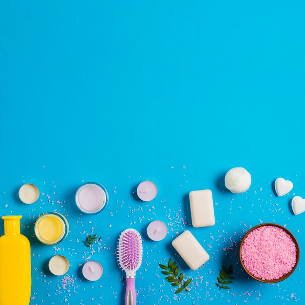 Pink salt; soap; cream and shampoo with different types of candles on blue backdrop