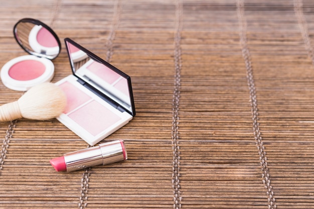 Free photo pink shade blusher palette; makeup brush and lipstick on placemat
