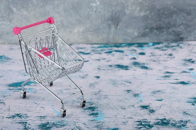 Pink shopping cart trolley on a marble background.