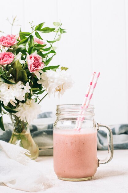 Pink smoothie next to vase with roses