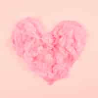 Free photo pink soft feather heart shape on peach colored background