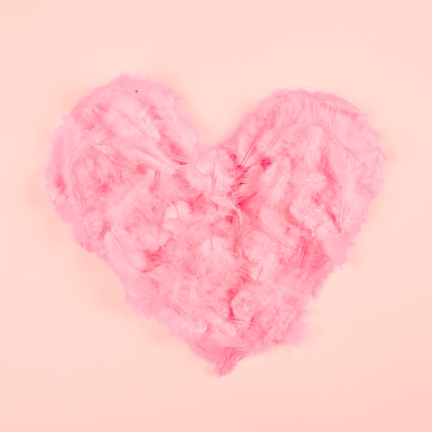 Pink soft feather heart shape on peach colored background