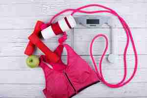 Free photo pink sport bra, red bars, thermomug, green apple, jump rope lie