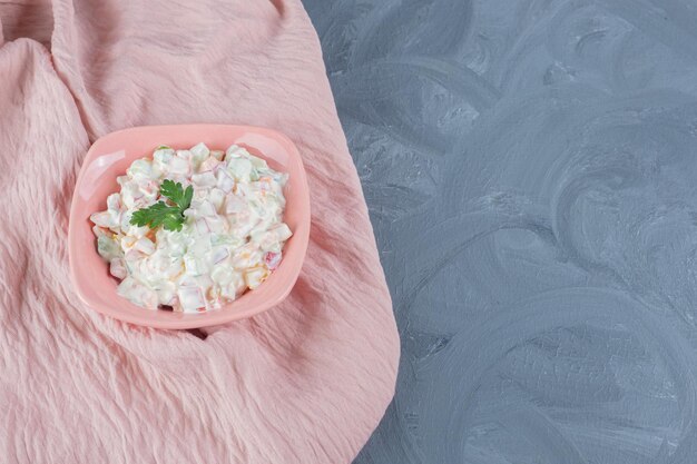 Pink tablecloth under a bowl of olivier salad on marble background. 